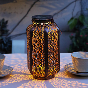 Lanterne solaire vintage à motifs fleuris avec une lumière chaude posé sur un support de jardin